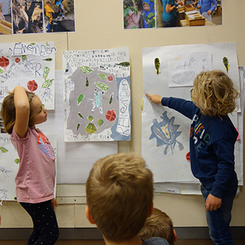 Young students pointing to drawings on a wall.