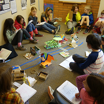 Students sitting in a circle on the floor examining various artifacts.