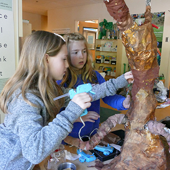 Two students working on a tree made from paper mache.