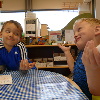 Two students shrugging and smiling at a classroom table.