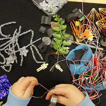 Student interacting with various objects: silver pipe cleaners, fake leaves, beads, and strings of various colors.