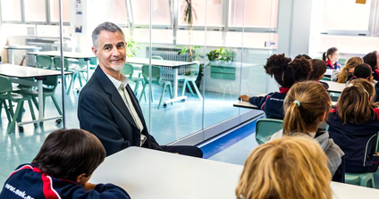 A man sits in a classroom with students who are listening to a lesson